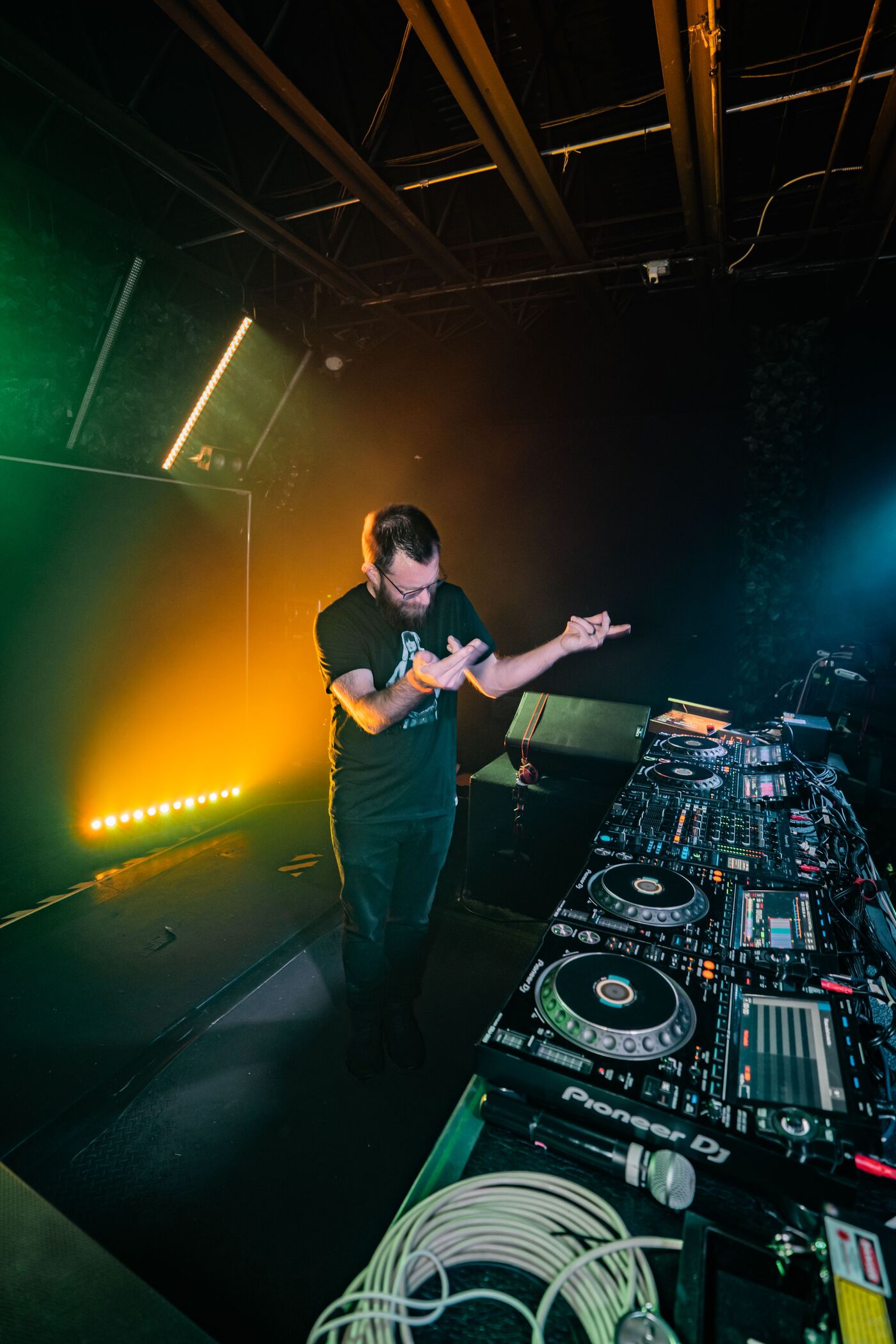 Sam behind the CDJs mid set, green and amber stage light filling the room